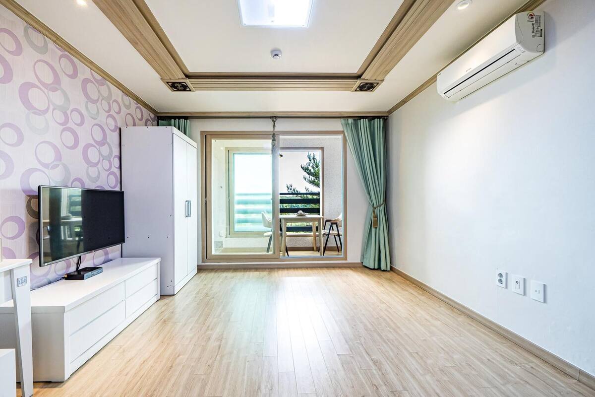 A modern living room with a flat-screen TV, white cabinetry, and a sliding glass door leading to an outdoor balcony.