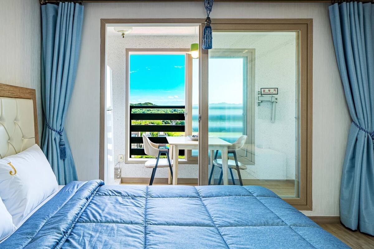 A bedroom with a bed, a view of a balcony, and a dining area.