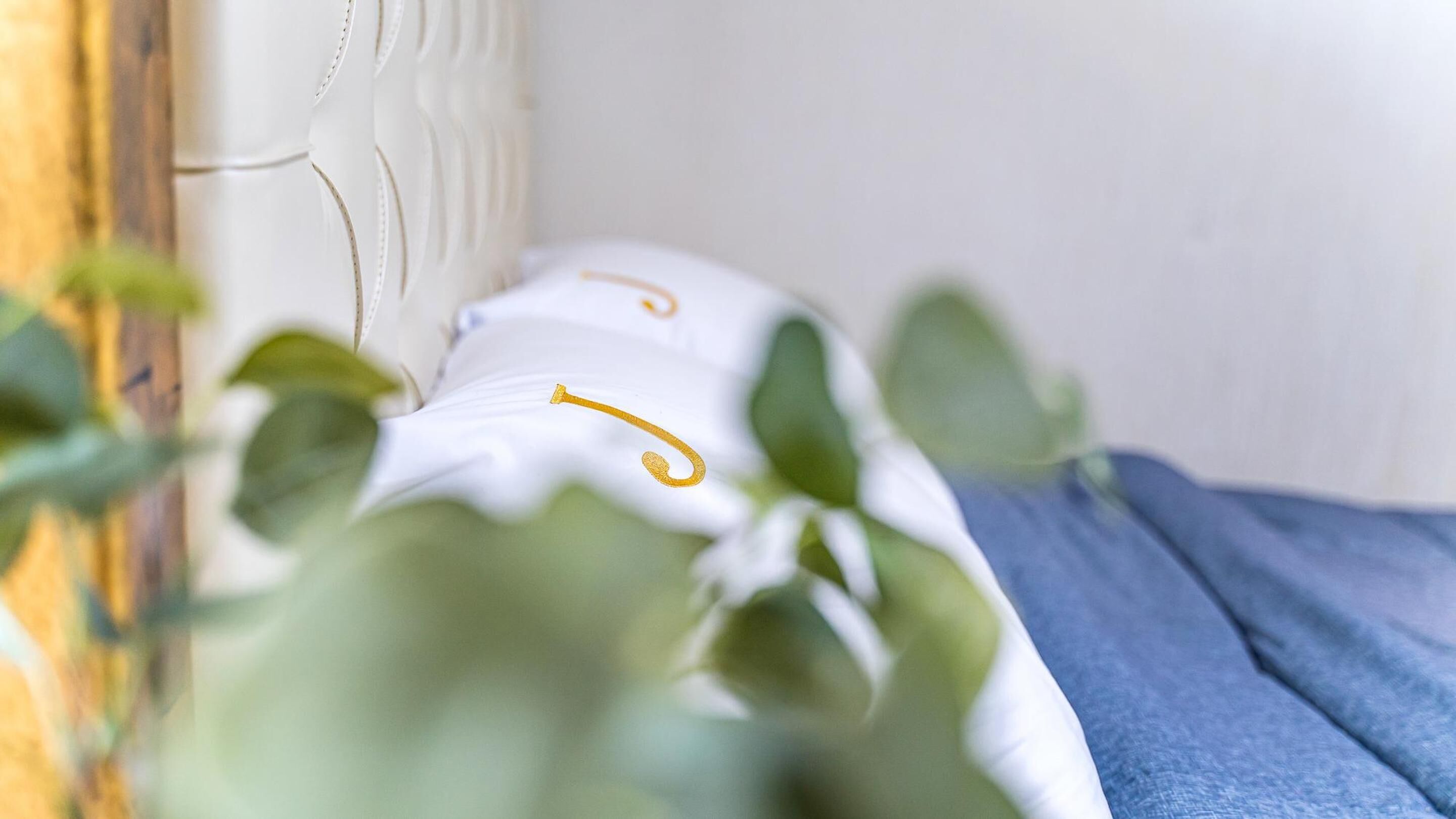 Una cama con ropa de cama blanca y una manta azul, parcialmente cubierta por follaje verde.