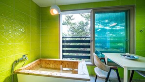 Un baño con una bañera de madera, una ventana con vistas a árboles, y una mesa con un frutero.