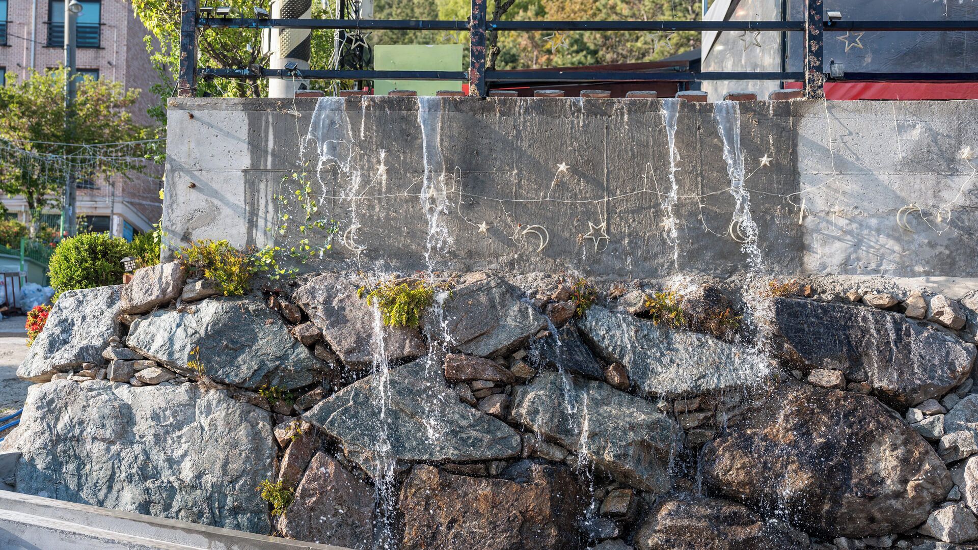 A stone wall with water cascading down, surrounded by rocks and vegetation.