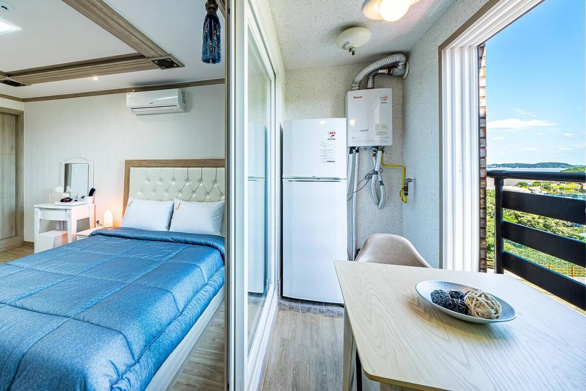 A bedroom with a bed, bedside table, and a view of a balcony with a table and a bowl of fruit.