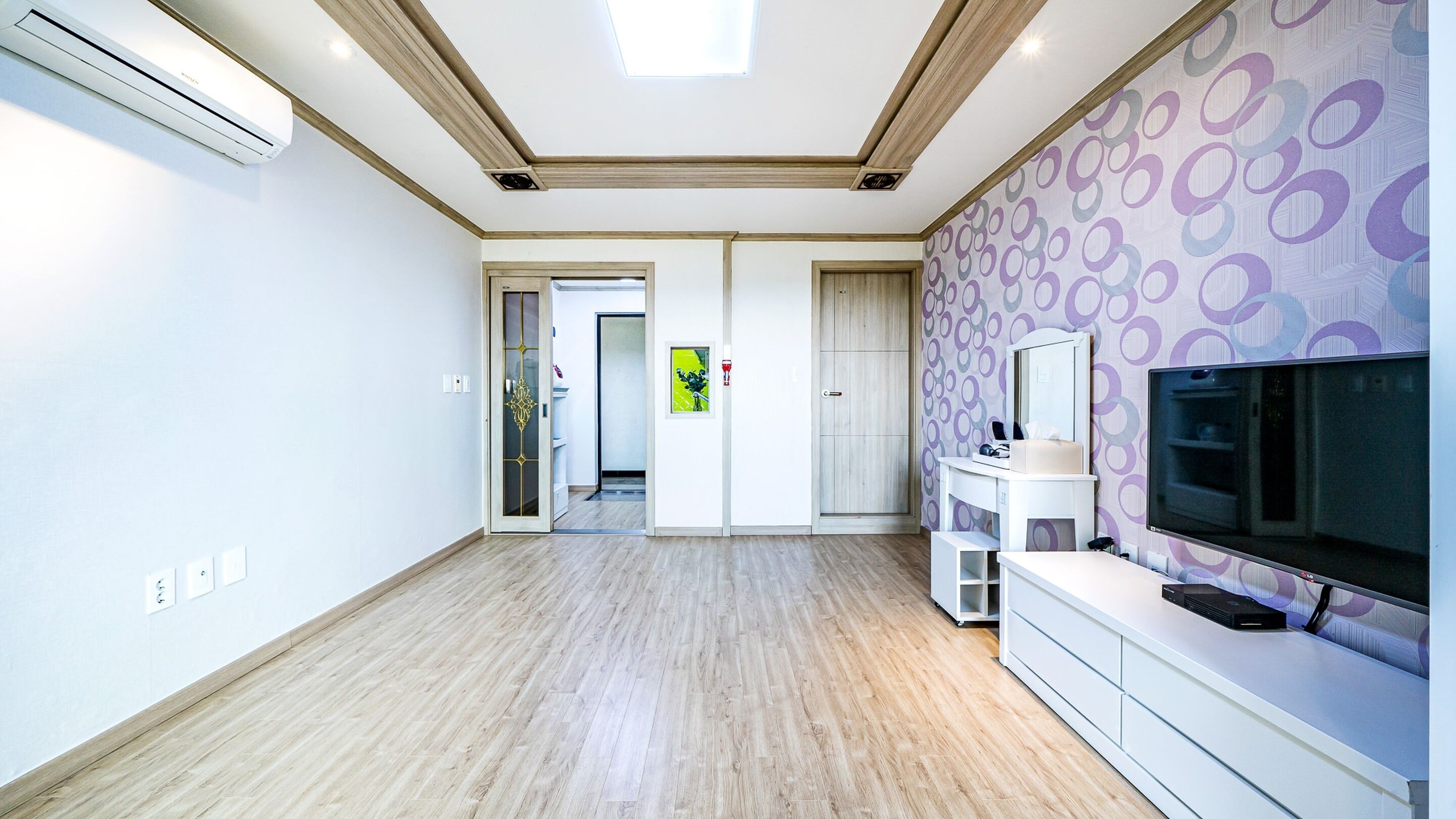 Un salon spacieux doté d’un grand téléviseur à écran plat, d’un meuble de rangement blanc et d’un papier peint à motifs.