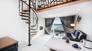 A modern interior with a spiral staircase, a sofa, a table with cups, and a view of the outdoors.