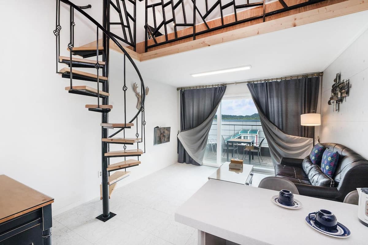 Ein modernes Interieur mit einer Wendeltreppe, einer Couch, einem Tisch mit Tassen und Blick ins Freie.