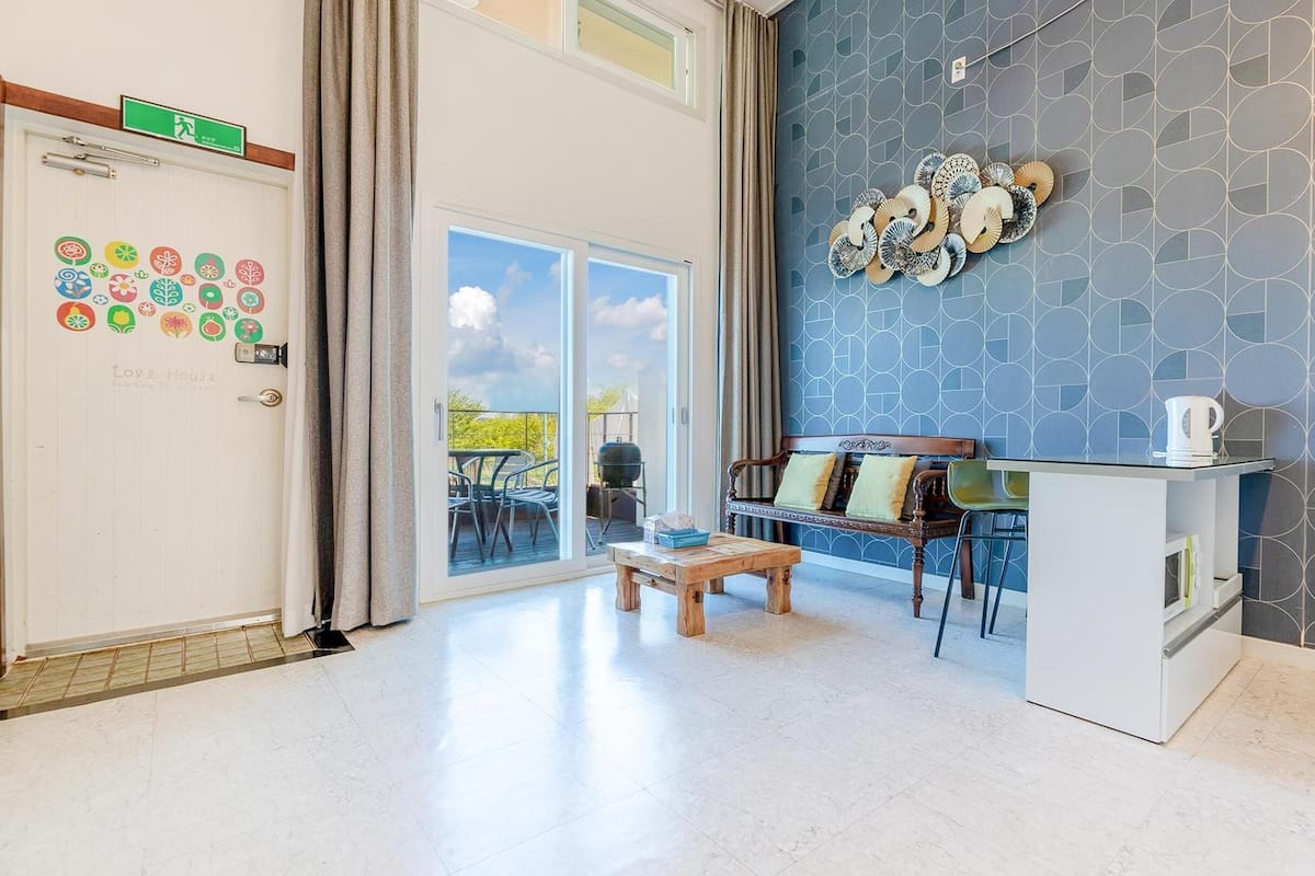 Ein modernes Wohnzimmer mit einem großen Schiebeglasfenster, das auf einen Balkon führt, einer Holzbank, einem Sofa und einem Couchtisch.