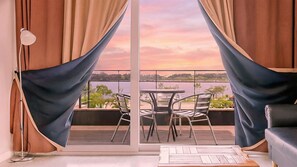A balcony with a table and chairs, curtains, and a view of a body of water during sunset. - Gangneung Olraeendaol Spa Pension (Gangneung)