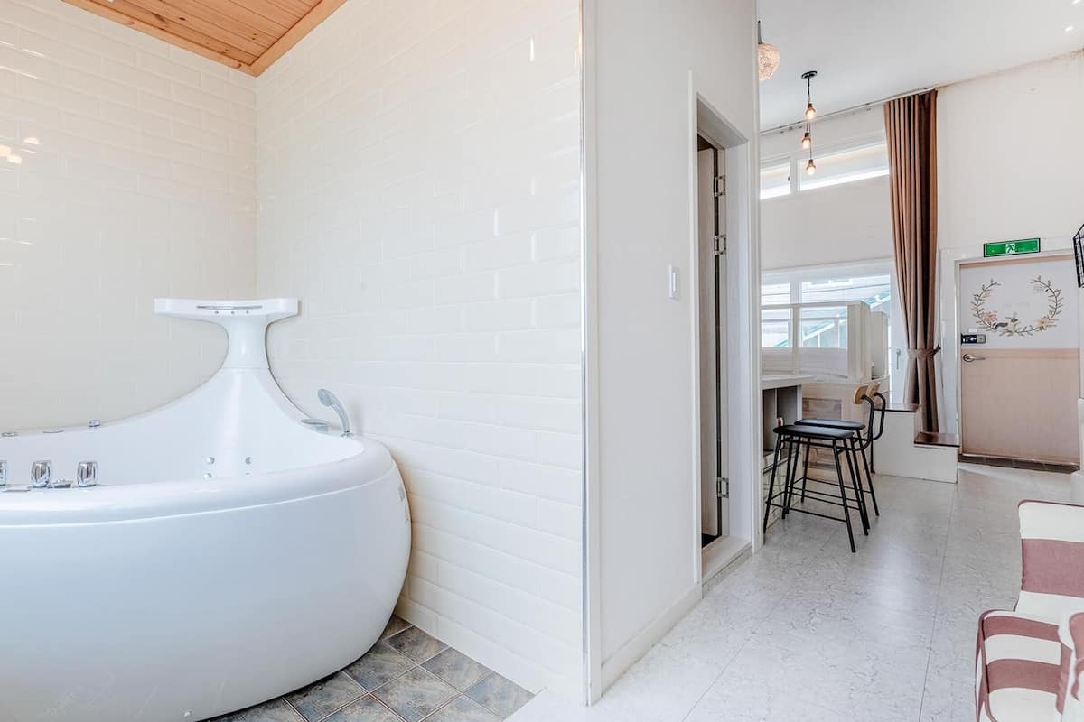 Ein modernes Badezimmer mit einer großen, freistehenden Badewanne, weißen Fliesenwänden und einer Holzbodenverkleidung.