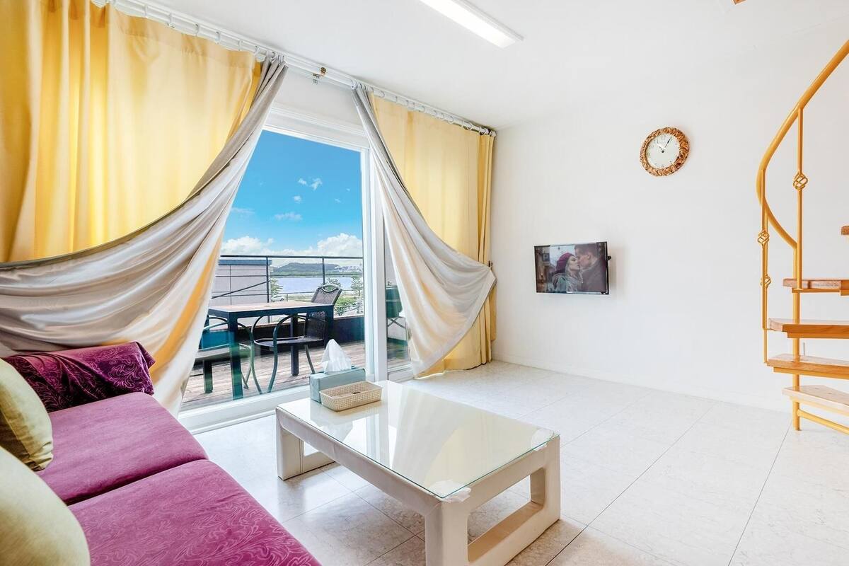Ein Zimmer mit einer Couch, einem Glastisch, einer Wendeltreppe, Meerblick und einem gerahmten Bild an der Wand.