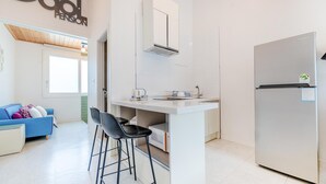 A compact kitchen with a built-in microwave, a refrigerator, and a small bar stool.