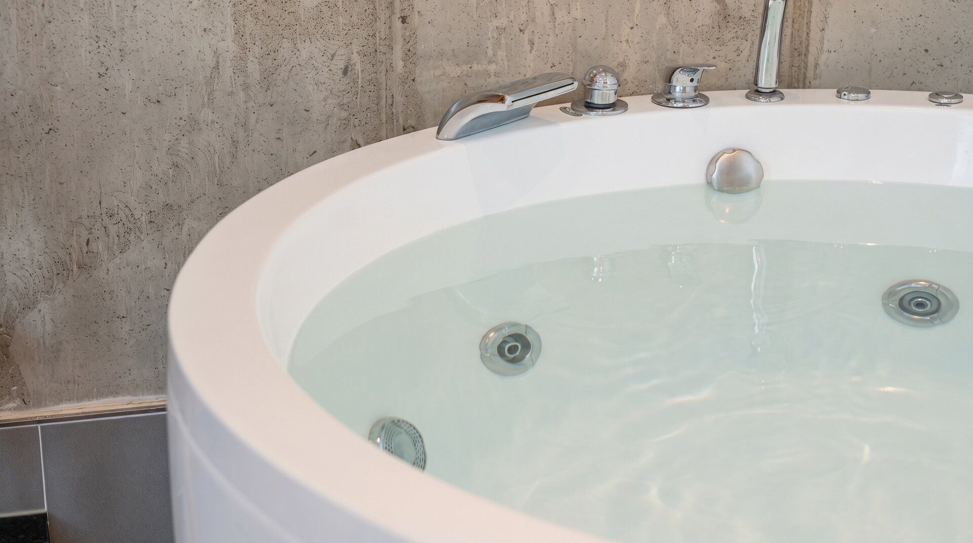 A bathtub with a faucet and control knobs, set against a textured wall.