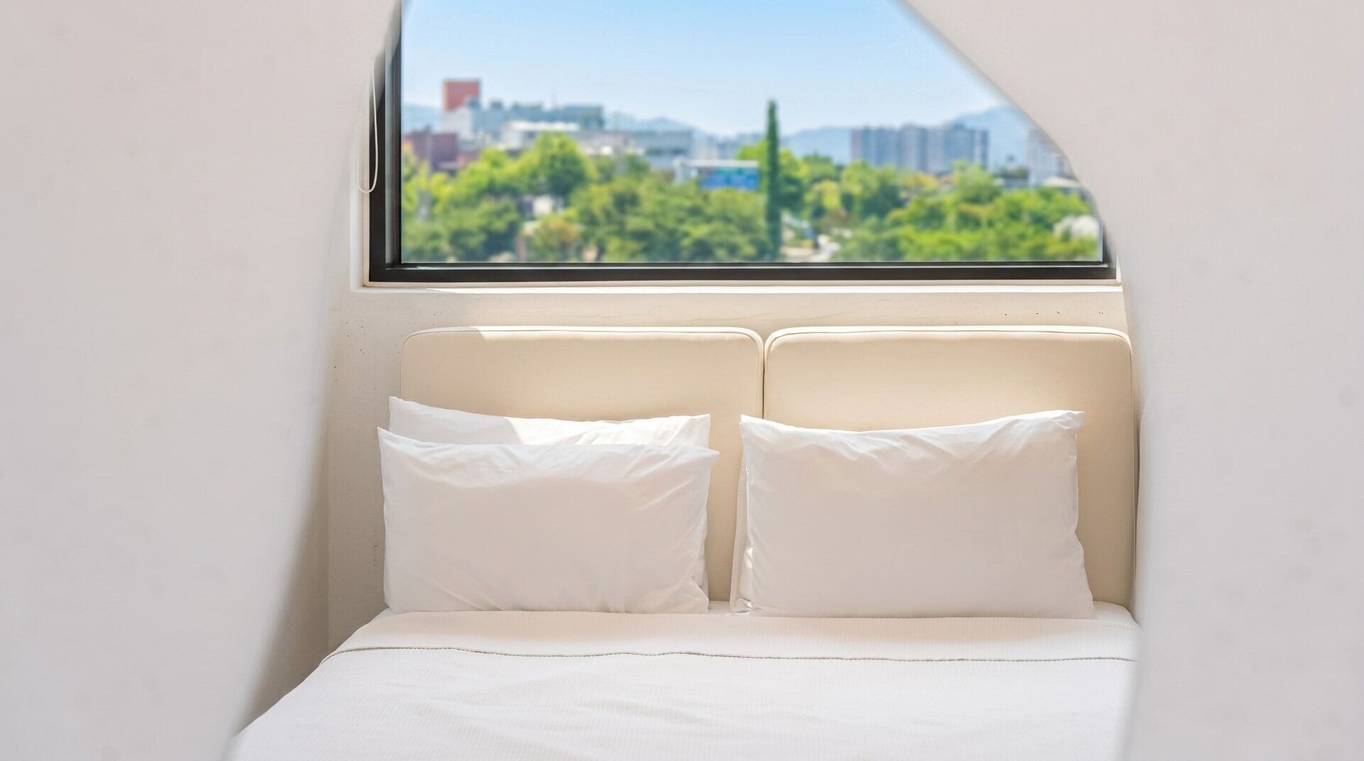 A bedroom with a bed, two pillows, and a window with a cityscape view.
