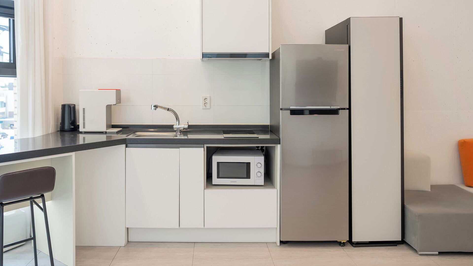 A compact kitchen with a built-in microwave, a stainless steel refrigerator, and a black countertop.