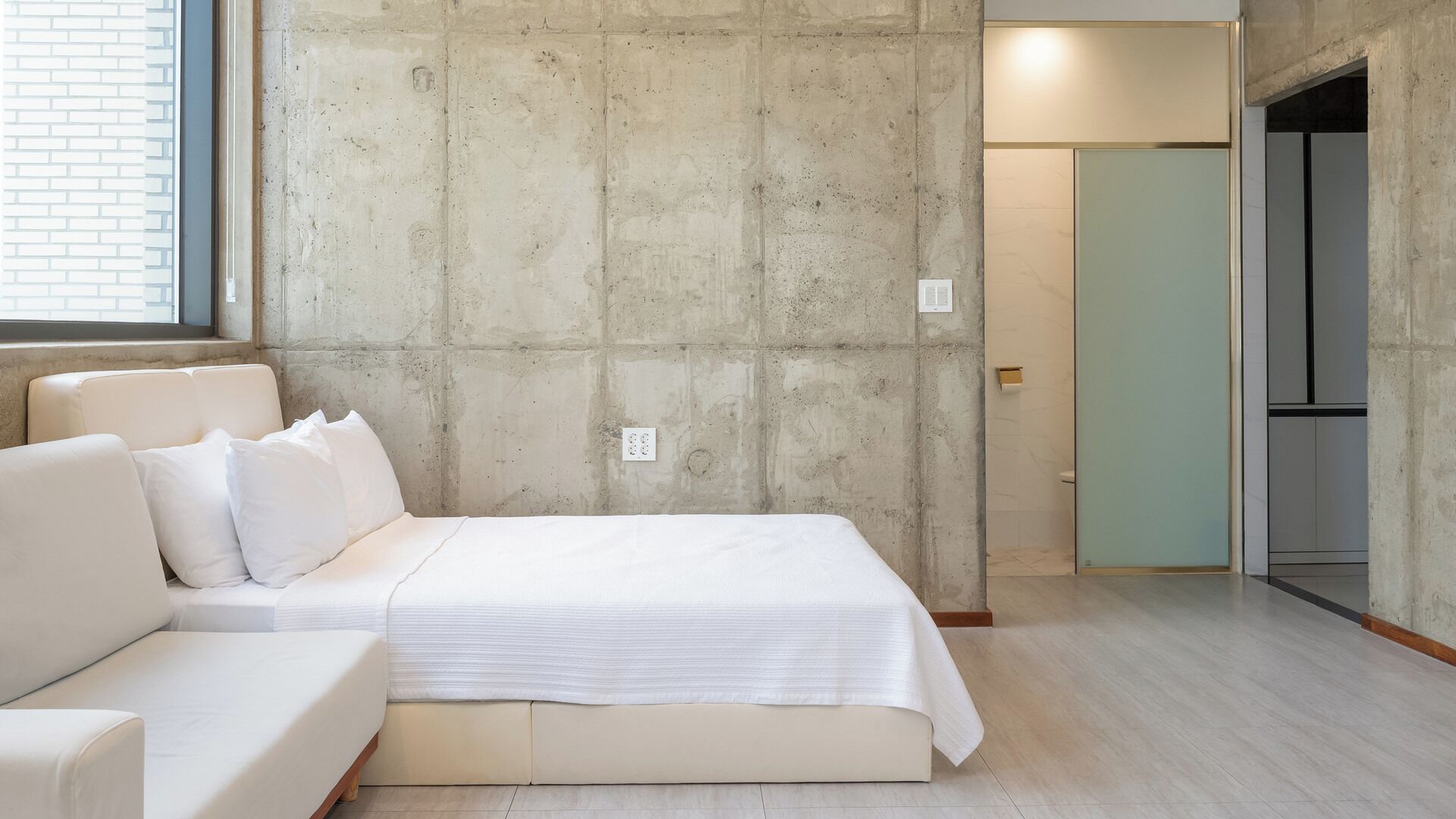 A room with a bed, a sofa, a window, and a door leading to a bathroom.