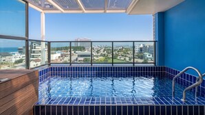 Ein Pool auf dem Dach mit Blick auf die Stadt, eine Holzbank und eine Glaseinfassung.
