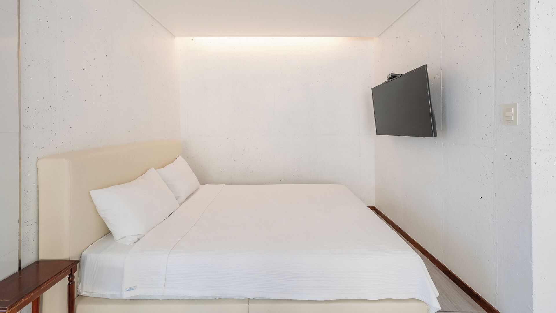 Ein Schlafzimmer mit einem Bett, einem Nachttisch und einem an der Wand befestigten Fernseher.
