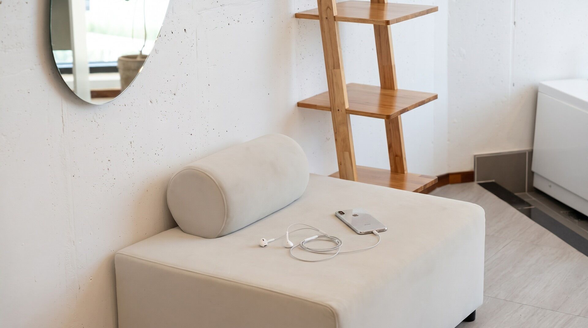 A clean, modern room with a white sofa, a round mirror, and a wooden shelf unit.