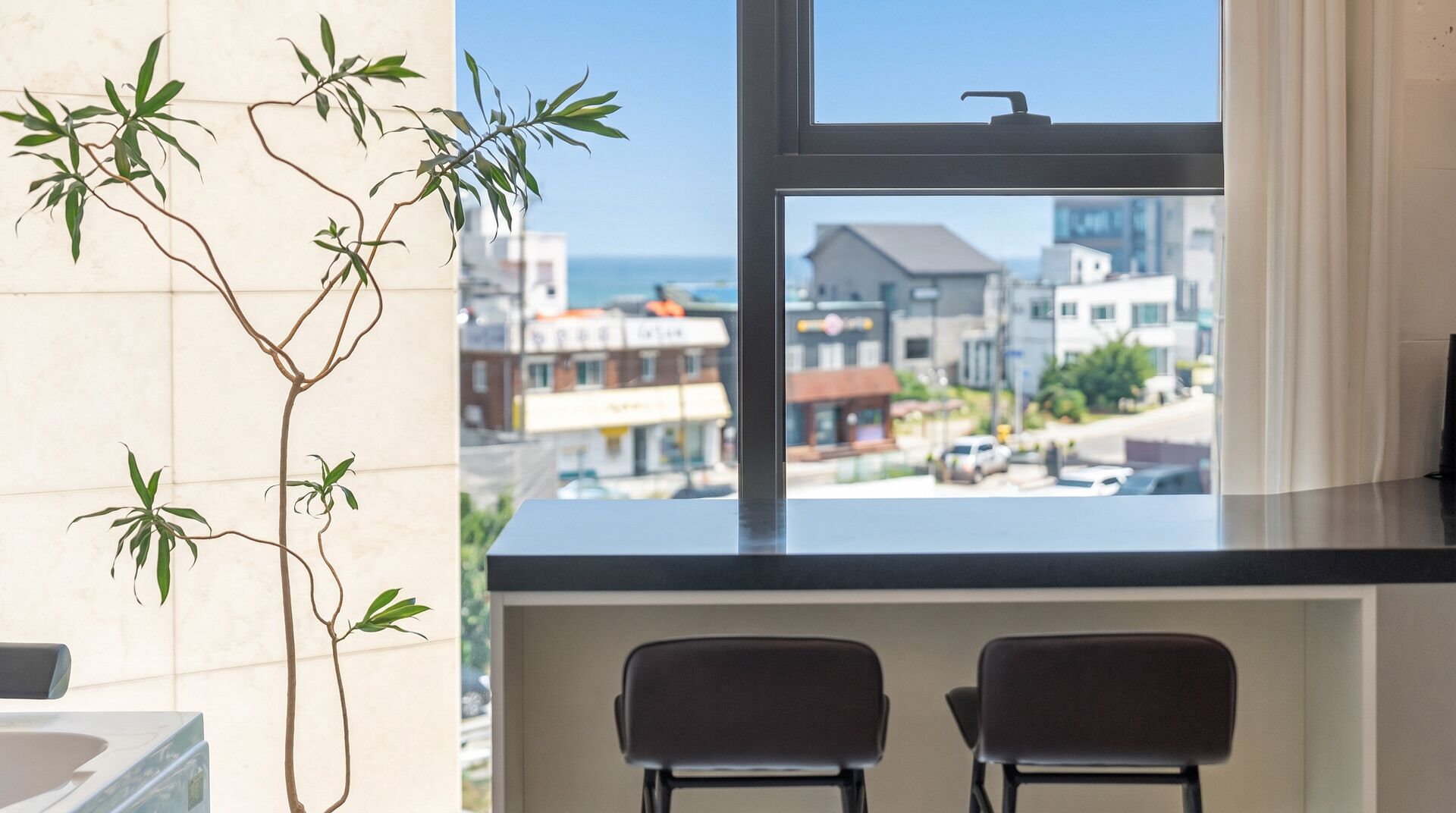 Habitación con vistas a un paisaje urbano a través de una ventana, dos sillas y una planta.