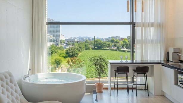 Ein modernes Badezimmer mit einer großzügigen Badewanne, einer Topfpflanze und Blick auf eine Stadtkulisse durch große Fenster.