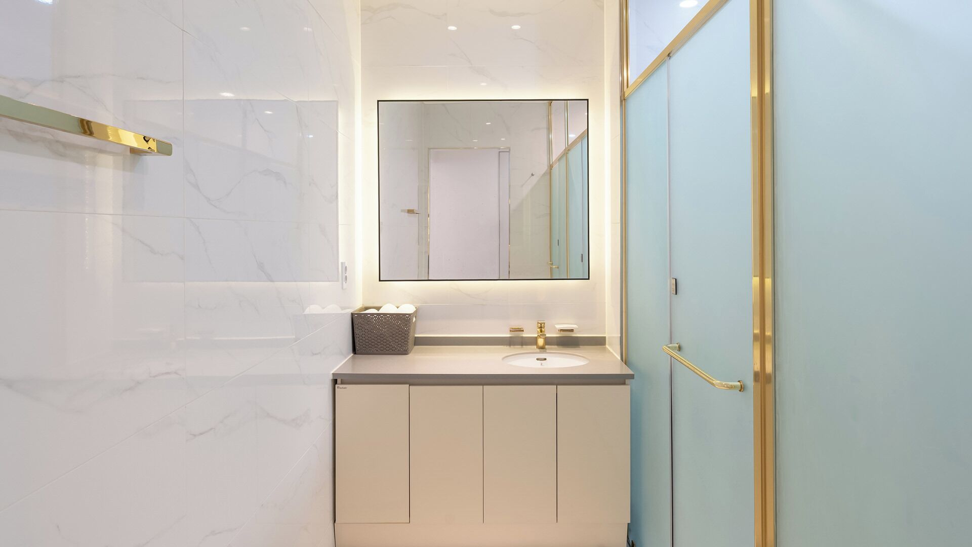 Un baño moderno con pared de mármol, un lavamanos con grifo dorado y un box de ducha de vidrio.