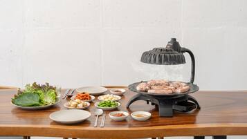 A table with a portable grill, various side dishes, and a white wall background.
