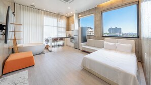 Ein modernes Hotelzimmer mit einem großen Bett, einer Badewanne, einem Essbereich und Blick auf die Stadt.
