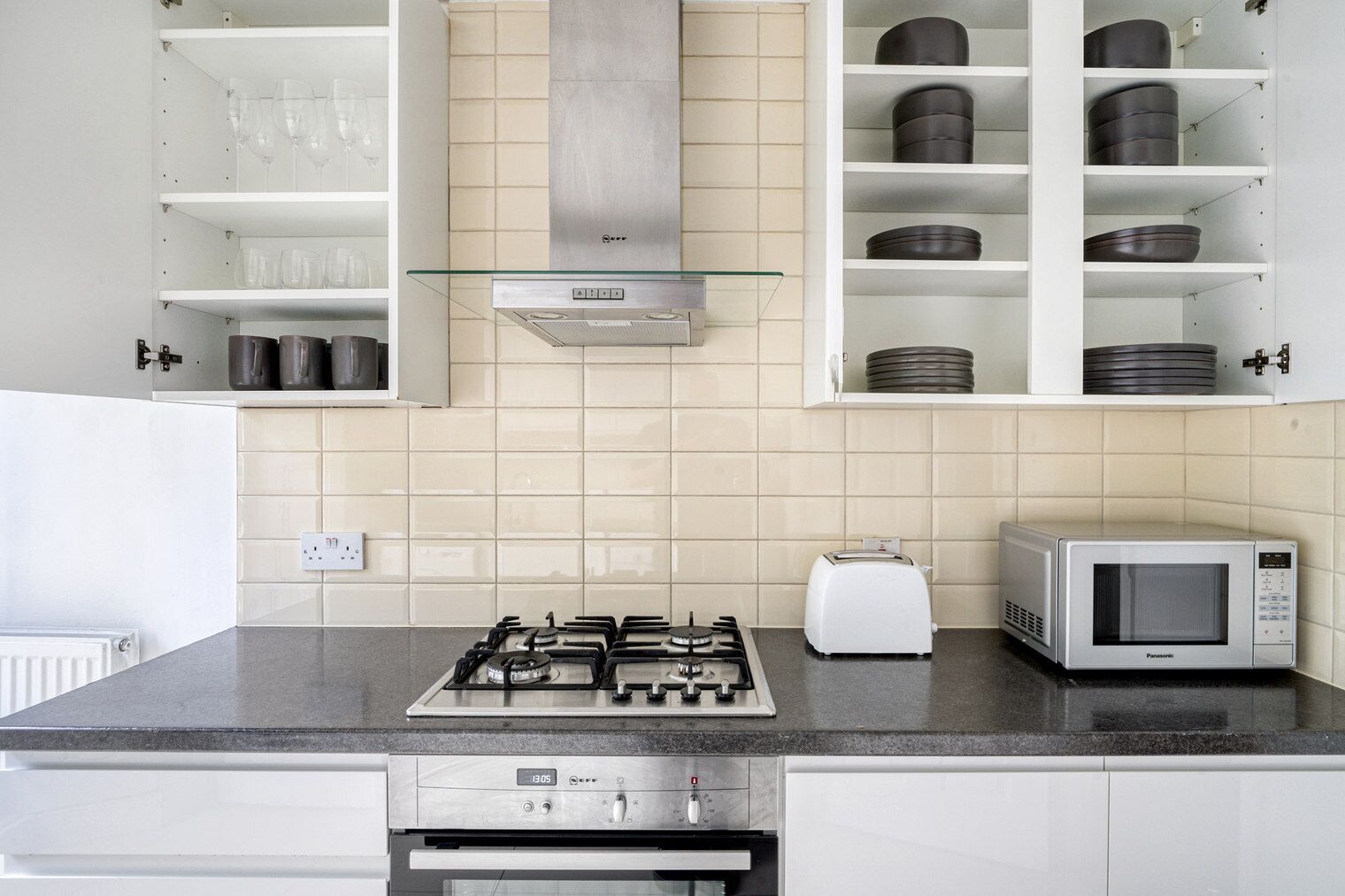 Una cocina moderna con estufa a gas, tostadora, microondas y repisas abiertas con utensilios de cocina.