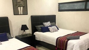 Habitación de hotel con dos camas, una mesita de noche con lámpara, una obra de arte en la pared y una ventana con persianas.