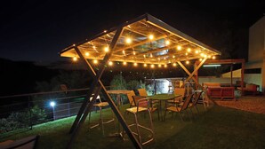 Un área de estar al aire libre con una pérgola de metal, luces colgantes y sillas.