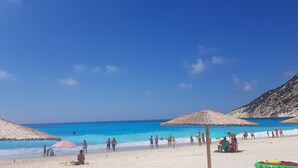 A beach with clear blue water, people sunbathing, and thatched umbrellas. - BlueTel Lixouri, Greece (Lixouri)