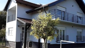 A two-story house with a balcony on the upper floor, a front door, and a small tree in front.