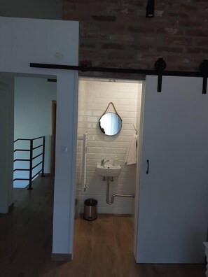 Bathroom features a round mirror, sink, and trash can, with a towel hanging on the wall.