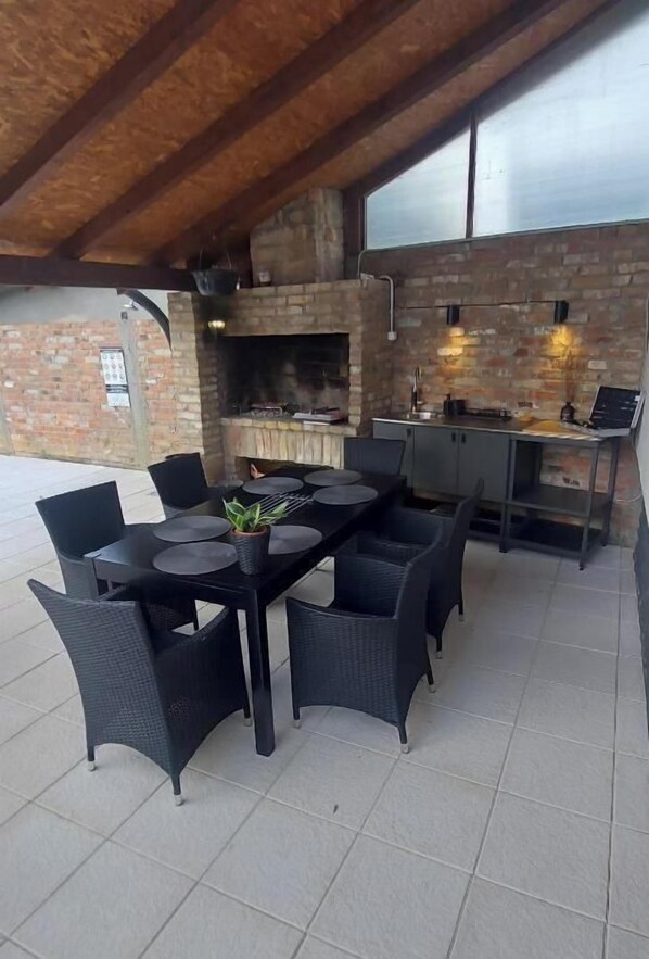 Une terrasse extérieure avec une cheminée en briques, une table à manger avec des chaises et un coin bar.