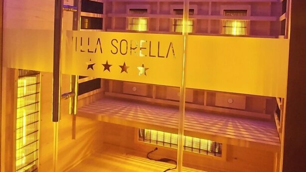 A room with a glass partition, a bed with a headboard, and a sign that reads "MILLA SORRELLA".