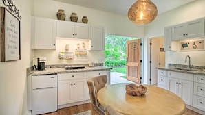 A kitchen with white cabinets, a granite countertop, a wooden dining table, and a hanging light fixture. - Rancho Santa Fe Casita - Gate Guarded Community! (Rancho Santa Fe)