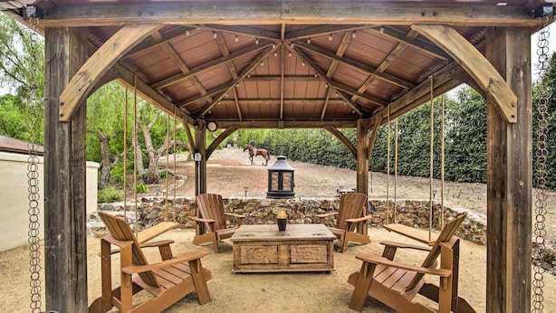 A wooden gazebo with a swing set, surrounded by chairs and a table, set in a garden with a horse in the background. - Rancho Santa Fe Casita - Gate Guarded Community! (Rancho Santa Fe)