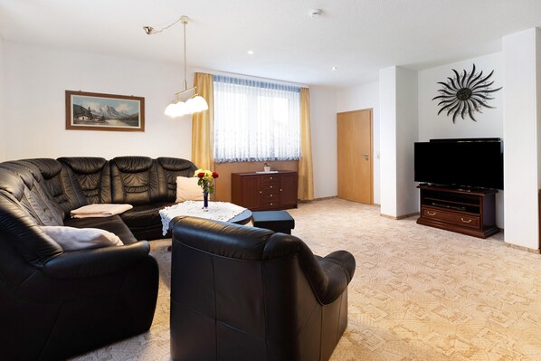 A living room with a sofa, a coffee table, a TV stand, and a painting on the wall. - Family-Friendly Apartment "Fuchsbaude" with Wi-Fi (Allrode)