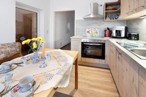 Una cocina con armarios de madera, estufa, cafetera y una mesa de comedor con mantel floral y flores amarillas.