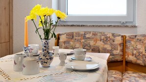 A dining table with a floral tablecloth, a vase with yellow flowers, and various white ceramic tea sets.