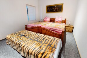 Ein Schlafzimmer mit Bett, Nachttisch, Holz-Kopfteil, einem Fenster mit Jalousien und einem Bild an der Wand.