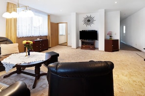 Ein Wohnzimmer mit einer Couch, einem Couchtisch mit weißer Tischdecke, einem Fernseher auf einem Schrank und einer Wanddekoration.