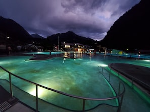 Una piscina de diseño curvo, rodeada por una barandilla, y un edificio con luces al fondo.