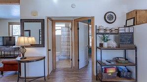Une chambre d’hôtel avec un plancher en bois, une télévision, une lampe, un miroir, une étagère avec des objets décoratifs et un panneau noir.