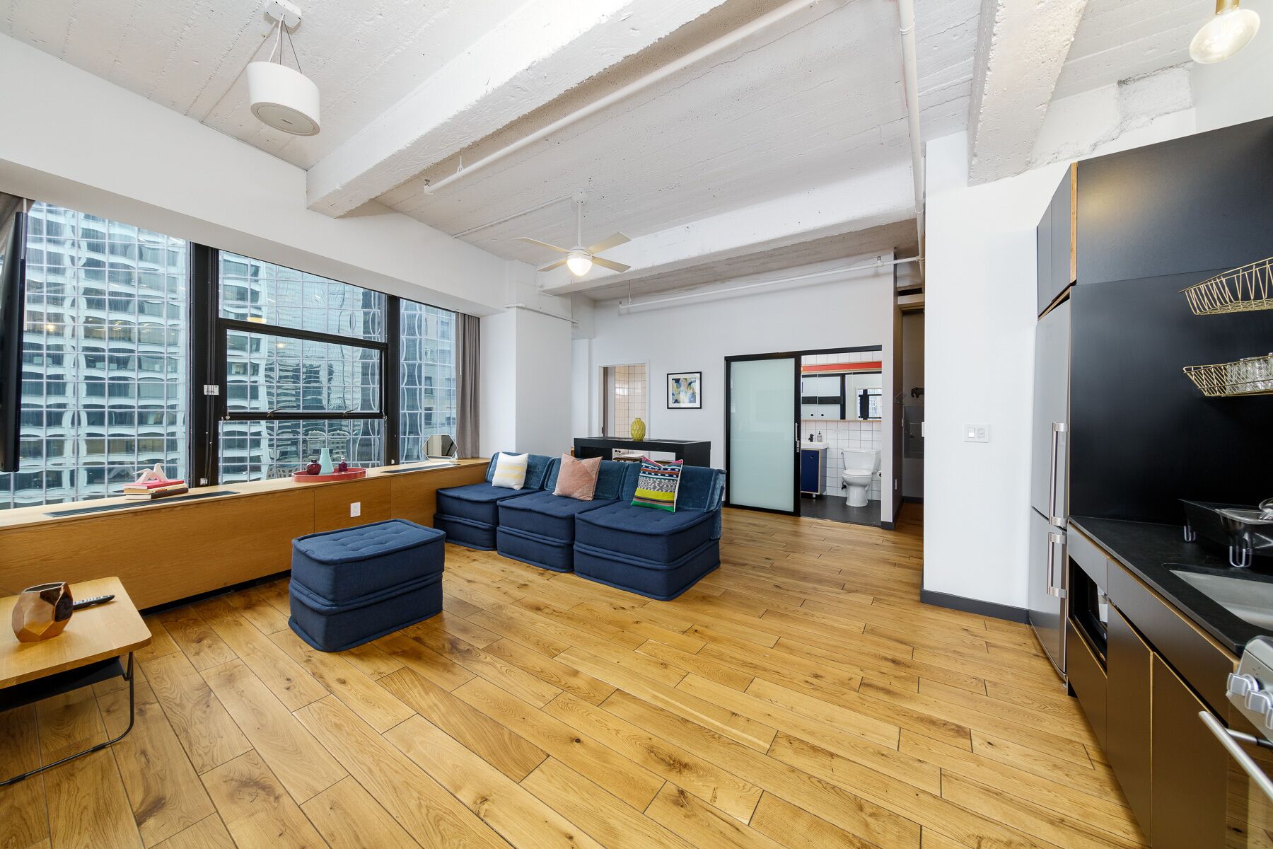 Un salon moderne avec un ensemble de canapés, un plancher en bois et une grande fenêtre donnant sur la ville.