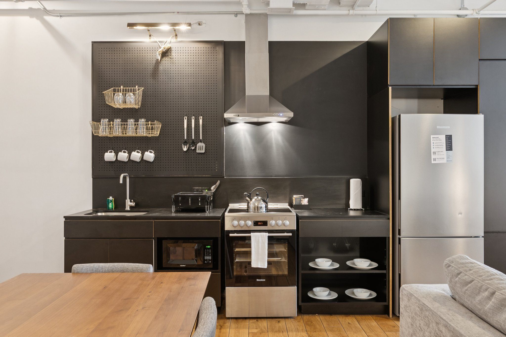 Una cocina moderna con estufa, horno y refrigerador de acero inoxidable, una mesa de comedor de madera y un sofá gris.