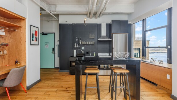 A modern kitchen with a central island, bar stools, and a view of the city through large windows. - Placemakr Wall Street (New York)