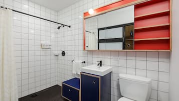 Un baño moderno con paredes de azulejos blancos, un inodoro blanco, un lavabo azul y negro, un espejo con marco rojo y una zona de ducha.