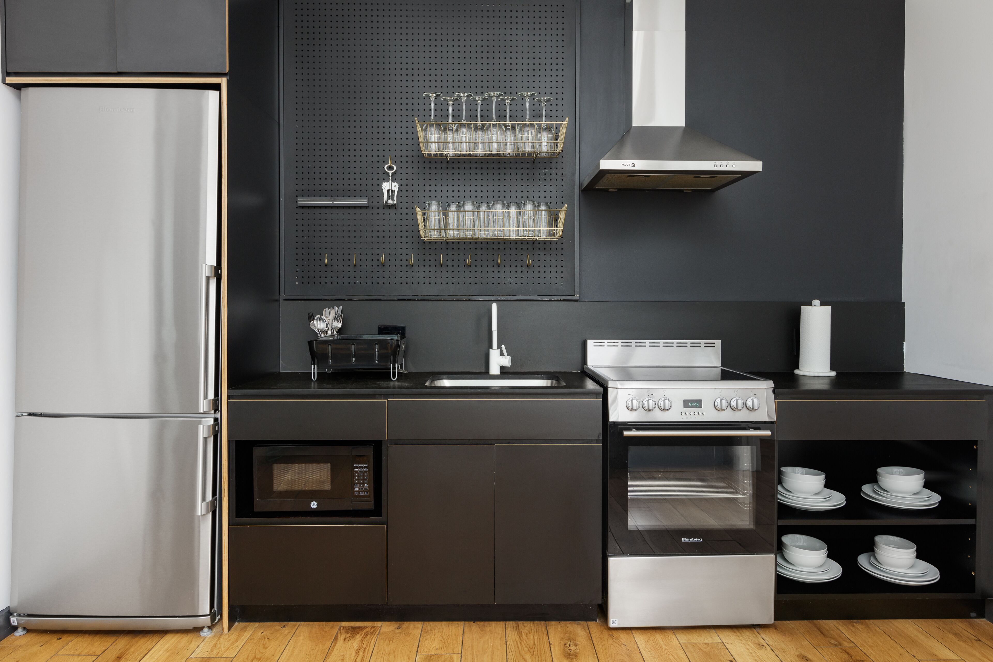 A modern kitchen with a stainless steel refrigerator, oven, microwave, and a wall-mounted wine rack.