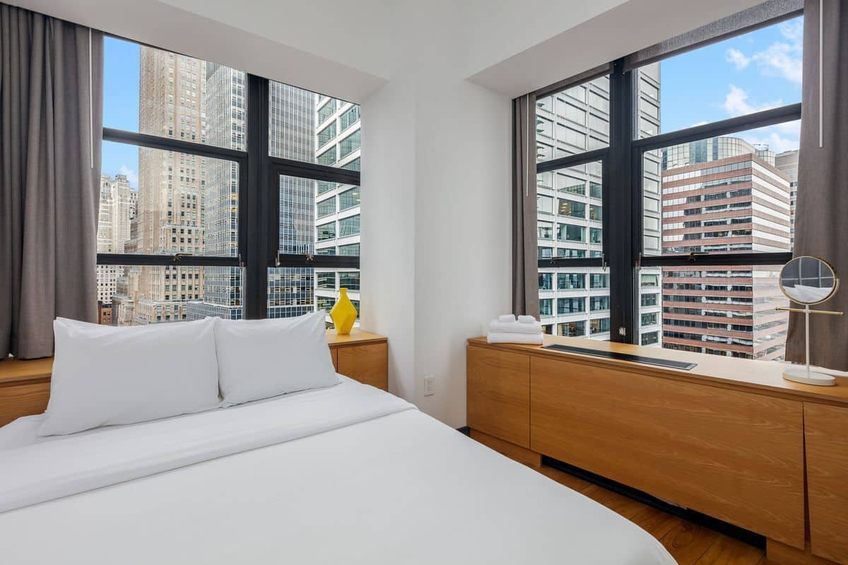 A hotel room with a large bed, wooden nightstands, a mirror, and a view of tall buildings.