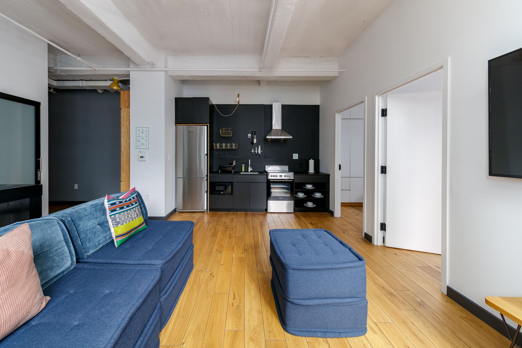 A modern living room with a blue sofa, a matching ottoman, and a kitchen area with a stove and oven.